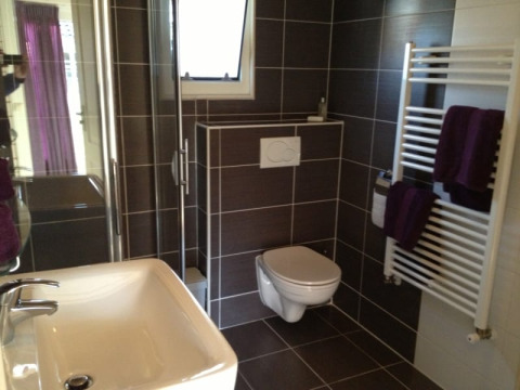 Moderne badkamer in een lodge met hangtoilet, glazen douchecabine, wastafel en handdoekradiator.