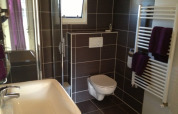 Salle de bain moderne dans un lodge avec toilettes suspendues, douche vitrée, lavabo et sèche-serviettes.