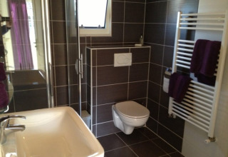 Salle de bain moderne dans un lodge avec toilettes suspendues, douche vitrée, lavabo et sèche-serviettes.