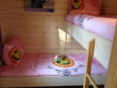 Acogedora habitación de una cabaña con literas de madera clara y ropa de cama rosa con estampados.