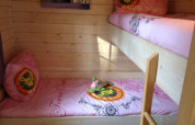 Et hyggeligt værelse i en lodge med køjesenge lavet af lyst træ og pink sengelinned med mønstre.