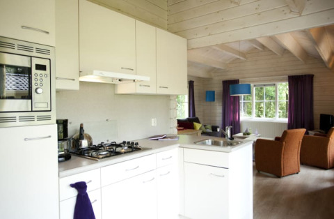 Moderne keuken en leefruimte in een gezellige lodge met lichte kleuren, houten balken en ruime ramen.