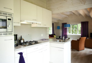 Moderne keuken en leefruimte in een gezellige lodge met lichte kleuren, houten balken en ruime ramen.