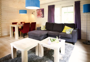 Woonkamer in een lodge met grijze bank, paarse gordijnen, rode stoelen en blauwe lampen.