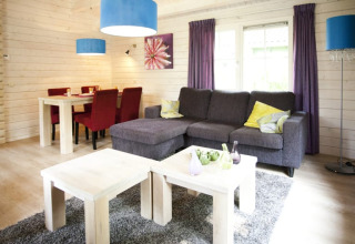 Lodge woonkamer met grijze zetel, paarse gordijnen, rode stoelen en blauwe lampen, lichte houtwanden.