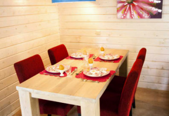 Eethoek in een lodge met houten wanden, gedekte tafel voor vier, rode stoelen en blauwe lamp.