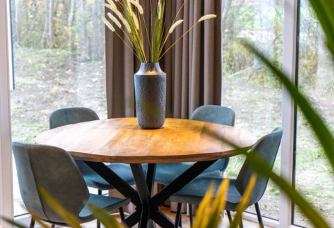 Rundt træbord med fire blå stole og en vase med dekorative græsser på Pavilion Lodge med udsigt til naturen.