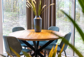 Ronde houten tafel met vier blauwe stoelen en een vaas met siergrassen in Pavilion Lodge, zicht op het groen.