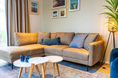 Gezellige woonkamer in Pavilion-lodge met hoekzetel, blauwe kussens, wanddecoratie en staande lamp.