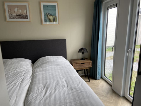 Slaapkamer in Pavilion lodge met tweepersoonsbed, nachtkastje, lamp, schilderijen en zicht op terras.