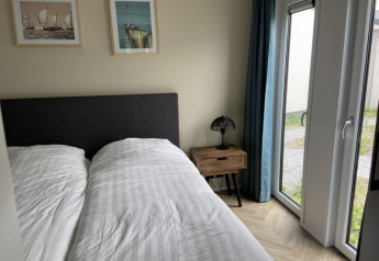 Dormitorio en la cabaña Pavilion con cama doble, mesita, lámpara, cuadros y vista a la terraza exterior.