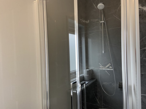 Cabine de douche moderne avec porte vitrée et carrelage sombre à la lodge Pavilion, lumière du jour visible.