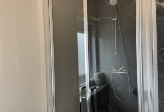 Cabine de douche moderne avec porte vitrée et carrelage sombre à la lodge Pavilion, lumière du jour visible.