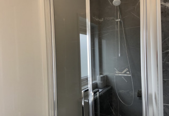 Cabine de douche moderne avec porte vitrée et carrelage sombre à la lodge Pavilion, lumière du jour visible.