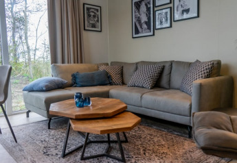 Gemütliches Wohnzimmer im Pavilion Lodge mit grauem Sofa, Kissen, Holztischen und Wandbildern.