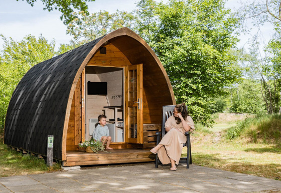 Una donna e un bambino si rilassano davanti a un lodge Trekkerspod a Kampeerdorp de Zandstuve, Paesi Bassi.