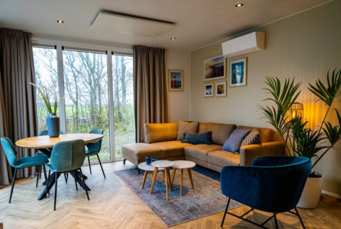 Modernes Wohnzimmer in der Pavilion-Lodge mit Sofa, kleinem Esstisch, Sesseln und Blick ins Grüne.