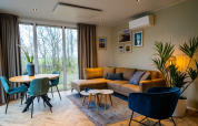 Sala moderna en el lodge Pavilion con sofá esquinero, silla azul, comedor y grandes ventanas al exterior.