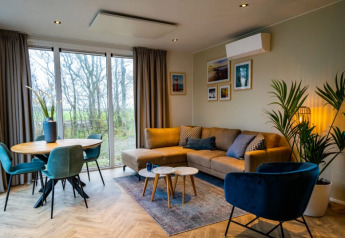 Sala moderna en el lodge Pavilion con sofá esquinero, silla azul, comedor y grandes ventanas al exterior.