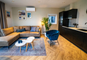 Lounge moderna della lodge Pavilion con divano angolare, poltrona blu, cucina e quadri decorativi.