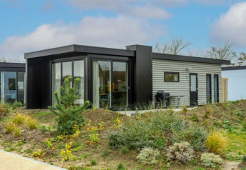 Lodge moderno con grandes ventanales y terraza, rodeado de vegetación natural bajo un cielo azul.