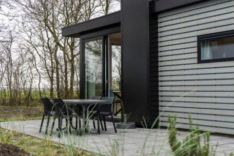 Moderne Pavilion-Lodge mit Terrasse, Tisch und vier Stühlen im Grünen neben Bäumen fotografiert.