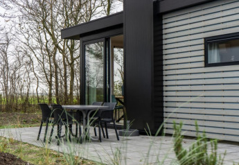 Lodge pavillon moderne avec table et quatre chaises sur terrasse extérieure, entouré d’arbres et nature.