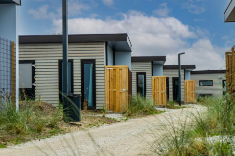 Reihe moderner Pavillon-Lodges mit Holzzäunen und Kiesweg, umgeben von grünen Pflanzen und Himmel.