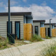 Række af moderne pavillonlodges med træhegn og grussti, omkranset af grønne planter og blå himmel.