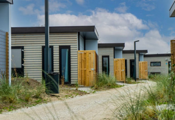 Reihe moderner Pavillon-Lodges mit Holzzäunen und Kiesweg, umgeben von grünen Pflanzen und Himmel.