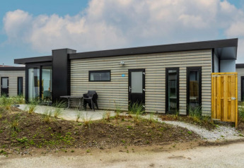 Moderno lodge Pavilion dal tetto piatto con rivestimento in legno e area esterna con tavolo e sedie, immerso nel verde.