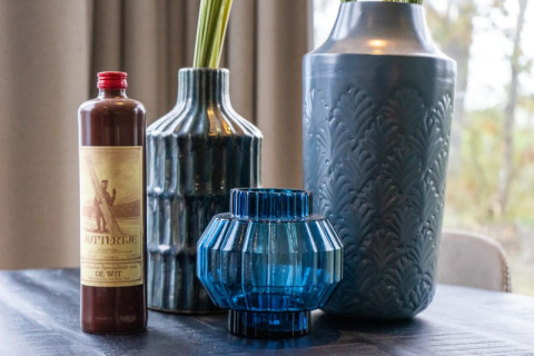 Decoratieve vazen en een fles met etiket op tafel in lodge Pavilion, met uitzicht op de natuur.