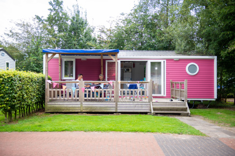 Pink Lodge XL cabin with a wooden deck and people relaxing on the porch, surrounded by greenery.