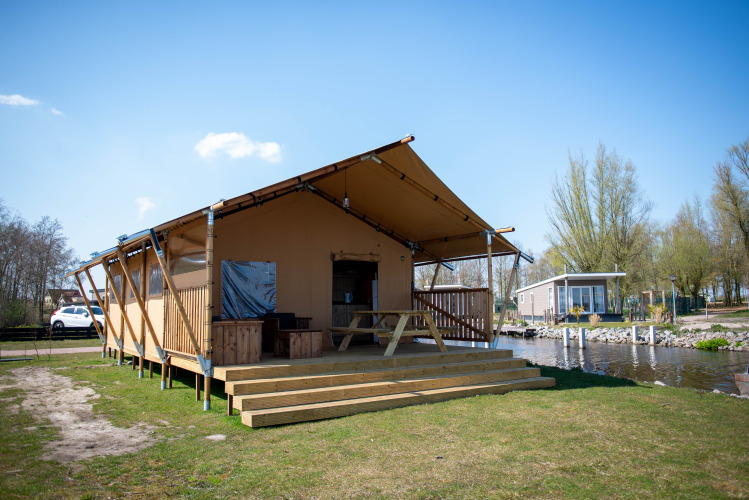 Safari-Zelt-Lodge mit Holzterrasse und Sitzbank, gelegen an einem Kanal in einer ruhigen Umgebung.