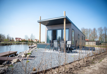 Vandlodge type 1 ved søen, moderne facade, udeområde med siddepladser og smuk natur omkring.