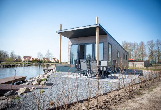 Vandlodge type 1 ved søen, moderne facade, udeområde med siddepladser og smuk natur omkring.