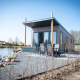 Vandlodge type 1 ved søen, moderne facade, udeområde med siddepladser og smuk natur omkring.