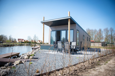 Waterlodge Typ 1 am See, modernes Gebäude mit Terrasse, Sitzbereich und ruhiger Umgebung.