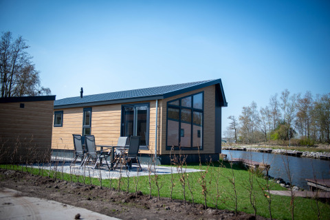 Wasserlodge Typ 2 mit stilvoller Holzfassade, großen Fenstern und Blick auf das Wasser bei Sonnenschein