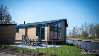 Moderne Waterlodge type 2 med stor vinduesfacade, terrasse og udsigt over vand i solrigt landskab