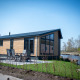 Modern Waterlodge type 2 with tall windows, patio seating, riverside view, and clear blue sky