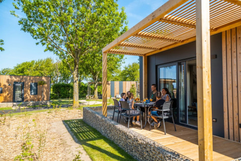 Familia disfrutando una comida en la terraza de una cabaña glamping moderna en parque vacacional soleado.