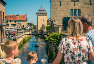 Gezin op brug met uitzicht op rivier en historische gebouwen in een vakantiepark met glamping.