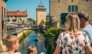 Familie genießt den Blick auf einen Fluss und historische Gebäude in einem Glamping-Ferienpark.