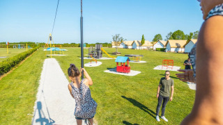 Kinder spielen auf einem Spielplatz in einem Ferienpark mit Glamping-Unterkünften und Hütten.