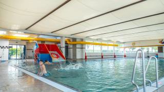 Hallenbad im Ferienpark mit bunter Rutsche, Kindern beim Spielen und großen Fenstern mit Außenblick.