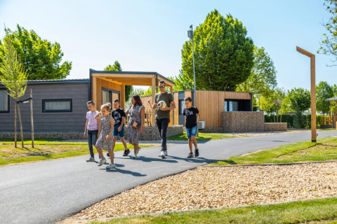 Famille se promenant dans un parc de vacances avec hébergements glamping modernes et arbres verts.