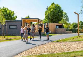Famiglia che passeggia in un villaggio vacanze con moderni alloggi glamping tra alberi verdi.