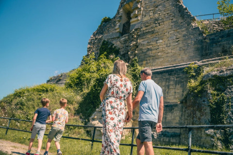 Familie udforsker gamle ruiner nær et glamping-opholdsområde under en klar blå himmel om sommeren.