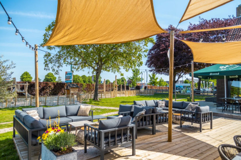Buitenlounge met comfortabele banken en schaduwdoeken bij een vakantiepark met glampingaccommodaties.